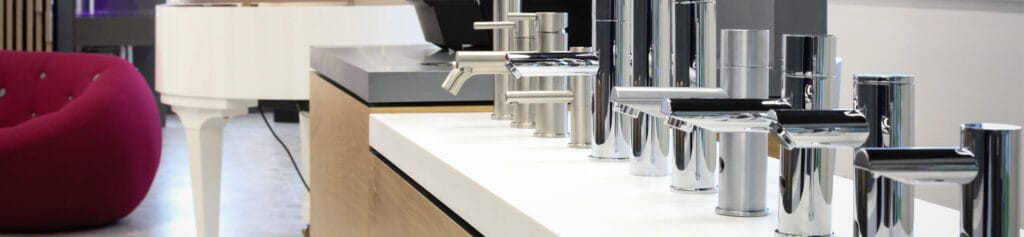 A row of various commercial washroom taps and counter top soap dispensers in satin finish and mirror polish stainless steel