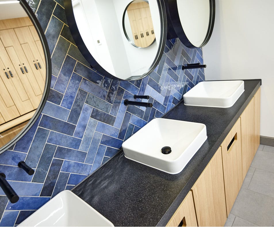 Row of rectangular white countertop basin designed with a black wash trough and washroom fittings