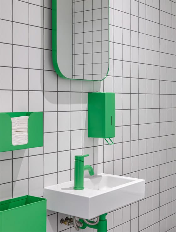 Light green sustainable coatings on washroom tap, soap dispenser, paper towel dispenser, mirror, and waste bin