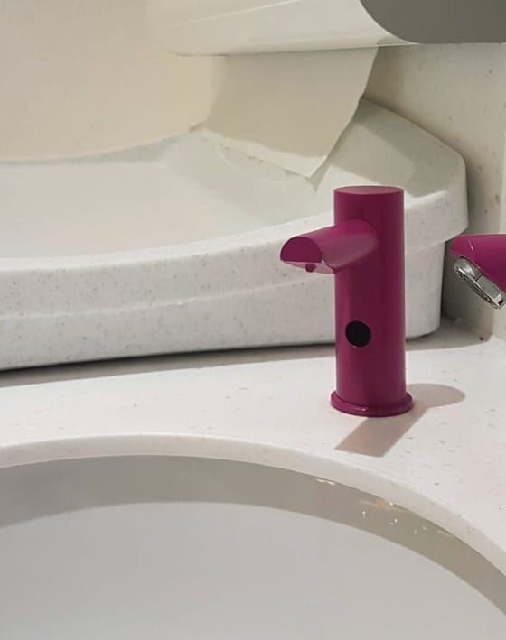 Purple finish counter-mounted touch free soap dispenser next to a commercial baby change table